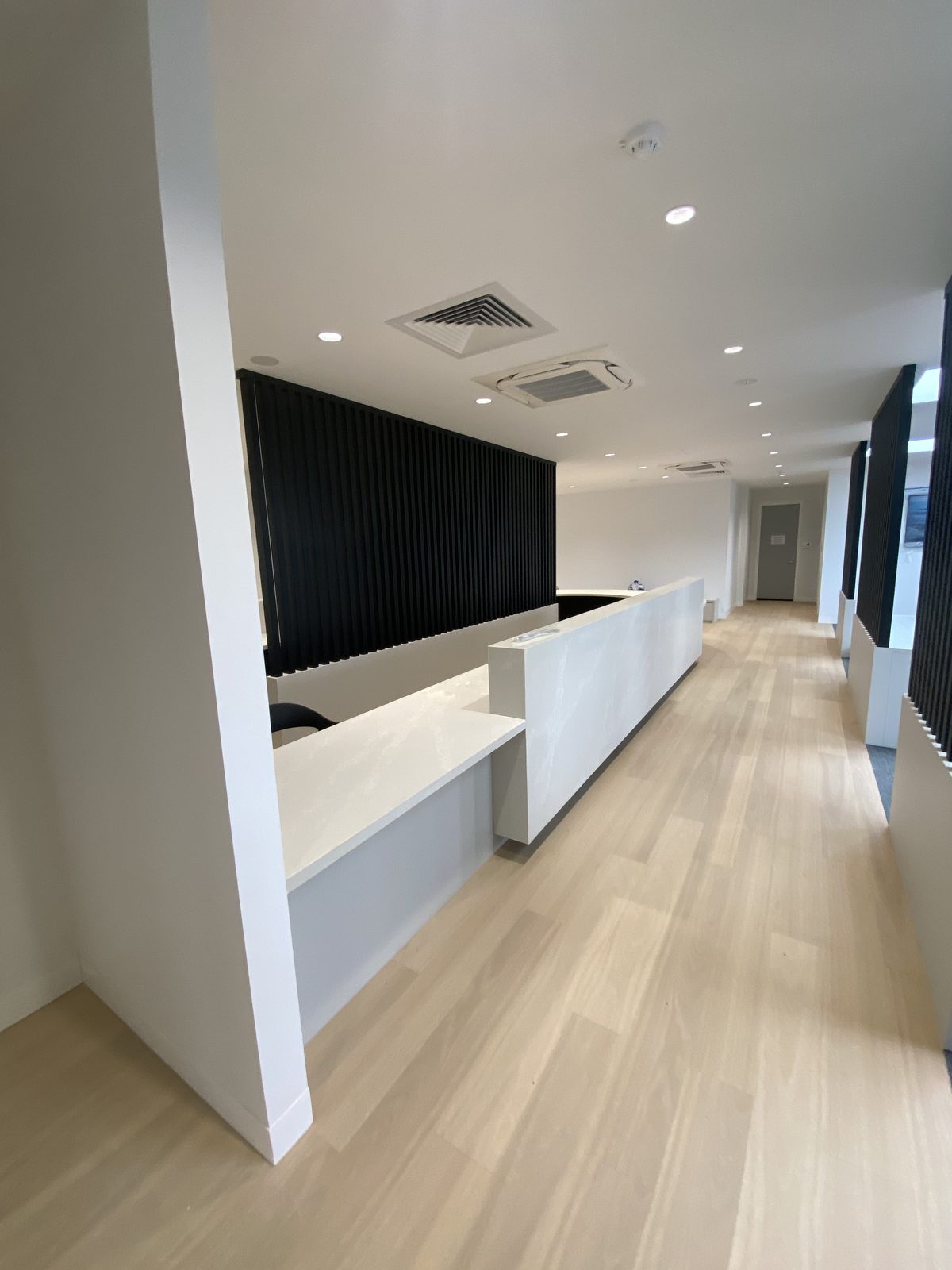 Completed medical centre reception with a long stone-topped counter against a black slatted timber screen, Bayside.